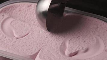 Close up view of a person scooping up fresh strawberry ice cream from tray. video