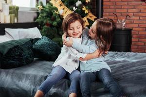 Playing and hugging each other. Kids sits on the bed with decorative background. Conception of new year