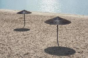 Two lonely reed umbrellas on an empty beach at noon under the sun photo