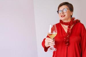 stylish mature senior woman in red blouse with glass of white wine celebrating new year. Fun, party, style, lifestyle, alcohol, celebration concept photo
