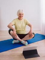 senior woman doing yoga online indoor. Anti age, sport, technology, yoga concept photo