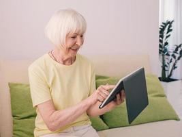senior cheerful caucasian stylish woman with gray hair with her tablet at home. Technology, emotions, family, healthy lifestyle, positive thinking concept photo