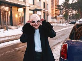 senior stylish woman in elegant black coat and hand bag walking from her car to business appointment. Business, style, anti age concept photo