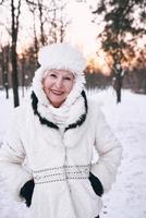 senior woman in white hat and fur coat enjoying winter in snow forest. Winter, age, season concept photo