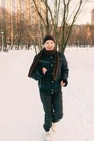 senior woman in hat and sporty jacket jogging in snow winter park. Winter, age, sport, activity, season concept