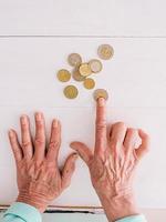 manos senior contando monedas de euro sobre la mesa. pobreza, crisis, depósito, concepto de recesión foto