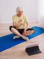 senior woman doing yoga online indoor. Anti age, sport, technology, yoga concept photo