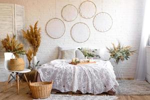 hermoso interior de la casa con tonos blancos y beige, con atrapasueños, flores secas y una cama foto