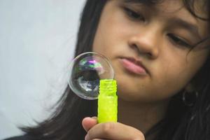 una niña que sostiene una máquina de hacer burbujas y las sopla. foto