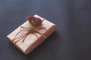 Craft gift box with knot natural with pink little flowers on black background. photo