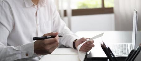 Cropped photo hand of man writing making list taking notes in notepad working or learning online with laptop at home