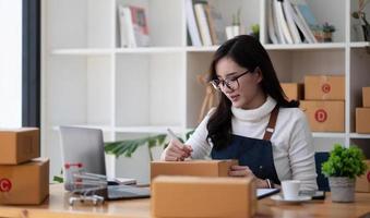 Young start up small business owner writing address on cardboard box at workplace.small business entrepreneur SME , working with box at home, Online selling, e-commerce, packing concept photo