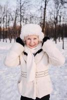 senior woman in white hat and fur coat enjoying winter in snow forest. Winter, age, season concept photo