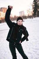 senior woman in hat and sporty jacket doing sports exercises in snow winter park. Winter, age, sport, activity, season concept