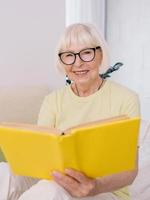 senior woman with gray hair reading a book on a sofa at home. Education, pension, anti age, reading concept photo