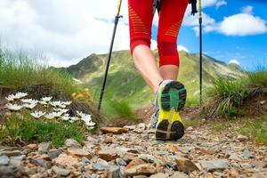 Detalle de piernas cerca de las flores de una niña que practica nordic walking en las montañas foto