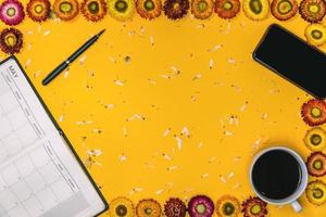 concepto de vista superior de fondo amarillo pastel. flores de colores que se disponen de forma con un bolígrafo y una taza de café colocadas. foto
