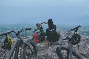 Asian lover women and men Travel Nature. Travel relax ride Mountain Bike in the wild. Sit down on a rocky cliff. Thailand