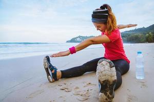 Asian women jogging workout on the beach. Sit down on the beach  fitness relax with stretch legs and Stretch arm. photo