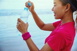 Asian women jogging workout on the beach in the morning. Relax with the sea walk and drinking water from the plastic bottles photo