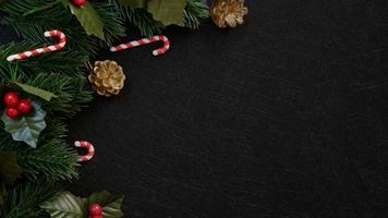 Vista superior de adornos navideños, hojas de abeto de pino, bastón de caramelo y frutos rojos sobre fondo de textura negro oscuro foto