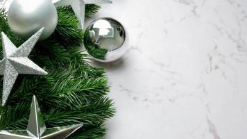 Hojas de pino verde sobre fondo de mármol blanco, adornos navideños en color plateado brillante. concepto de navidad simple y creativo. foto