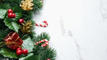 Green pine tree leaves, red christmas decorations and candy canes on white marble background, christmas decorations in bright red color. Simple and creative christmas concept. photo