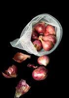 Red onions in mesh bag and some on floor isolated on black background photo