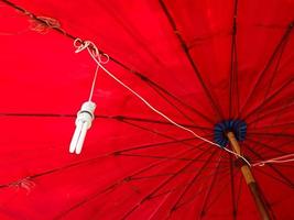 A compact fluorescent lamp hanging under a red umbrella photo