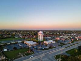 aerial view of urban area with water tower prominent in city wide highway large industrial area with parking lot single-family homes in background sun starting to set photo
