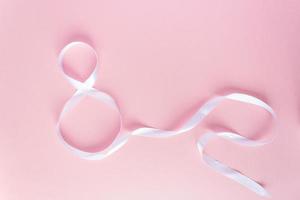 White gift celebration ribbon in 8 digit shape over pink background photo