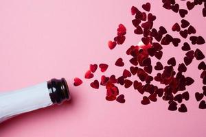 Champagne bottle with heart-shaped sequins on pink background. Valentines day concept. photo