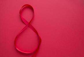 Satin red ribbon in the form of 8 on a red background photo