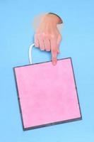 Female hand holding pink paper bag on blue background photo