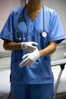 enfermera en uniforme azul claro poniéndose guantes estériles, sosteniendo un estetoscopio. foto