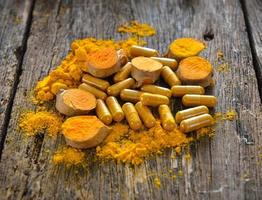 Turmeric powder and turmeric capsules on wooden background