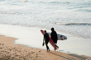 Young couple walking on the beach with their surf boards looking for the right spot to start surfing. Sunset, San Lorenzo beach, Gijon, Asturias, Spain photo