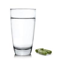 Vaso de agua y pastillas de cápsula de moringa sobre fondo blanco. foto