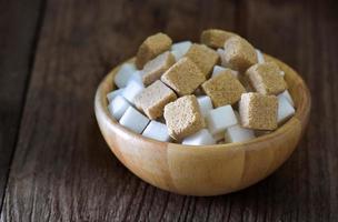 Terrones de azúcar en un tazón de madera sobre la mesa de madera foto