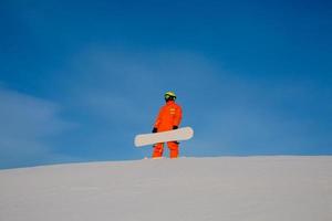 Snowboarder freerider con snowboard blanco sentado en la parte superior de la pista de esquí foto