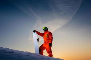 Snowboarder en la parte superior de la pista de esquí en el fondo de la hermosa puesta de sol
