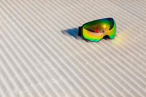 Ski goggles laying on a new groomed snow and empty ski slope photo