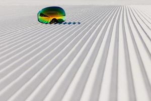 Gafas de esquí recostado sobre una nueva nieve arreglada y pista de esquí vacía foto