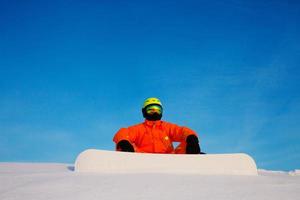 Snowboarder freerider con snowboard blanco sentado en la parte superior de la pista de esquí foto