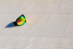 Gafas de esquí recostado sobre una nueva nieve arreglada y pista de esquí vacía foto