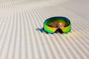 Gafas de esquí recostado sobre una nueva nieve arreglada y pista de esquí vacía foto