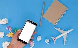 hand hold smartphone with airplane model and paper note on blue background.