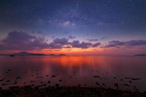 imagen de larga exposición de espectacular puesta de sol o amanecer, nubes del cielo sobre el mar tropical y la galaxia de la vía láctea. foto