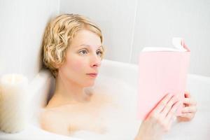 Mujer joven relajándose en el baño y leyendo un libro foto