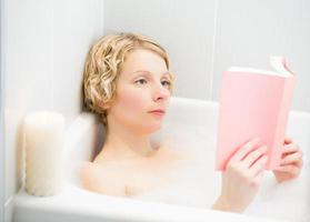 Mujer joven relajarse y leer un libro en el baño. foto
